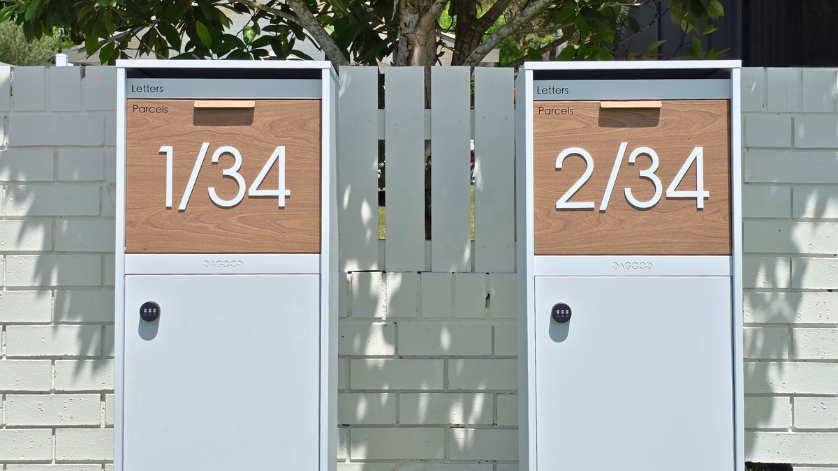 Two white Dagood parcel letterboxes with timber-look doors, numbered 1/34 and 2/34, in front of a painted brick fence