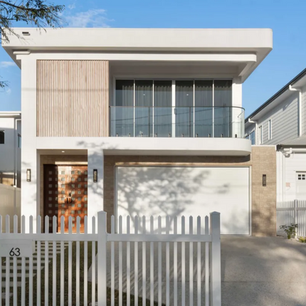 Modern two-story house with a white exterior and gray roof, surrounded by trees and a clear blue sky.