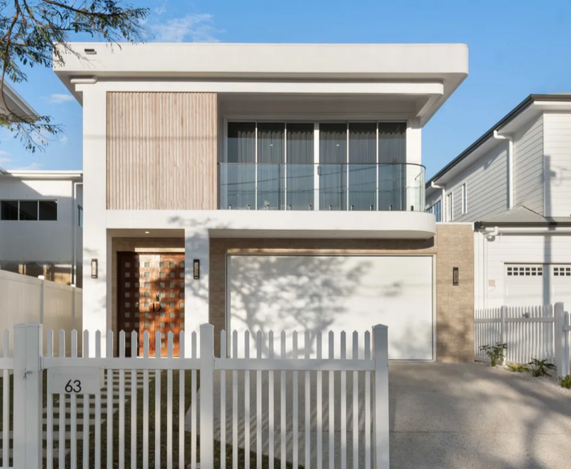 Modern two-story house with a white exterior and gray roof, surrounded by trees and a clear blue sky.